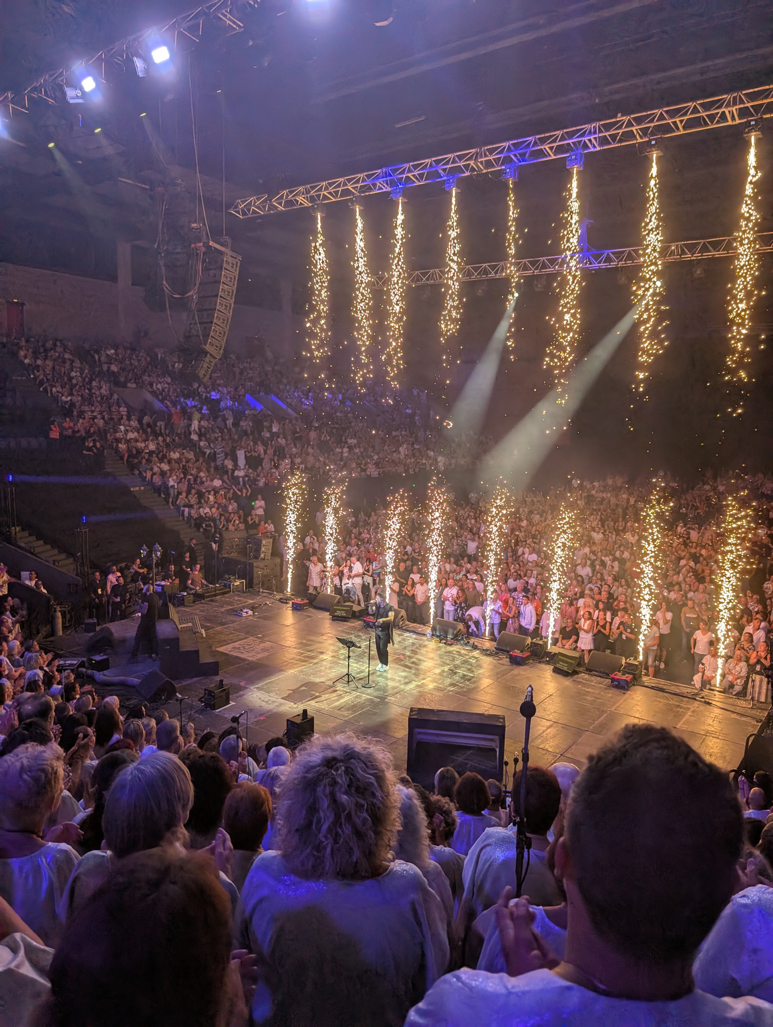Photo du concert de Le Choeur du Sud au Zénith de Toulon prise du point de vue des choristes avec Frank Castellano sur scène éclairé par de la pyrotechnique